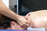 A female therapist applying massage with her thumbs on the neck of a woman lying down.