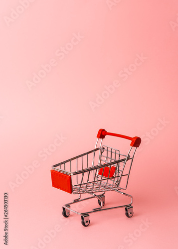 Women's shopping: an empty miniature trolley from a supermarket on a pink background.