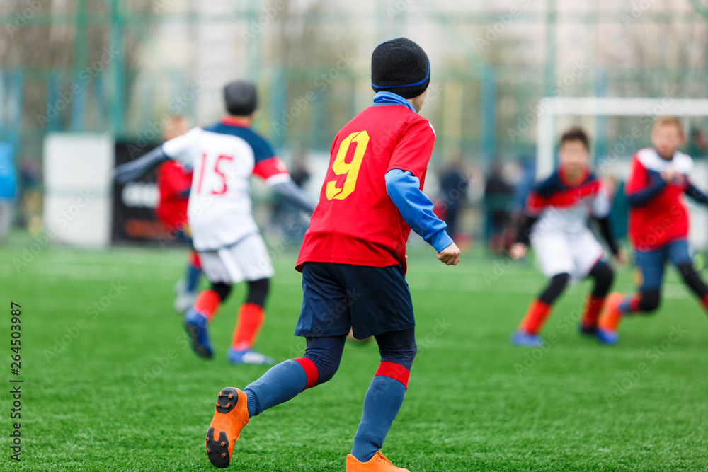 Boys kick soccer ball. Footballers run after the ball on green grass. Kids in white and red shirts dribbling, improve skills. Training, football, hobby, active lifestyle Boys kick soccer ball. Footballers run after the ball on green grass. Kids in white and red shirts dribbling, improve skills. Training, football, hobby, active lifestyle