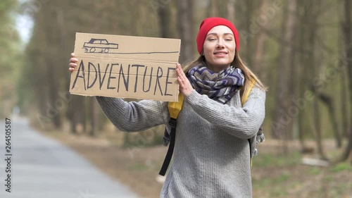 Pretty  smiling hitchhiking  girl on road with poster adventure. Travel life photo