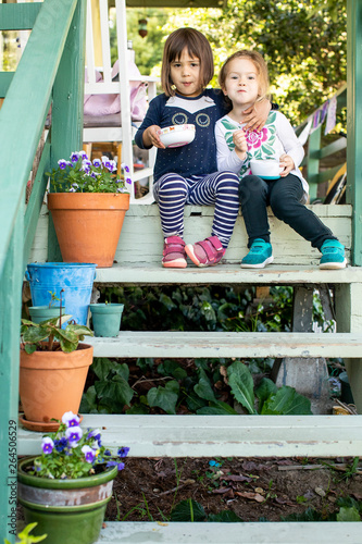 Two young girls sitting on a porch together eating a snack.