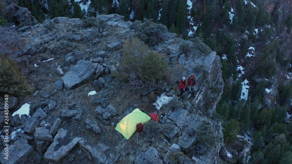 Aerial view of campsite on cliff looking down American Fork Canyon as couple sits on the ledge at dusk. Aerial view of campsite on cliff looking down American Fork Canyon as couple sits on the ledge at dusk.