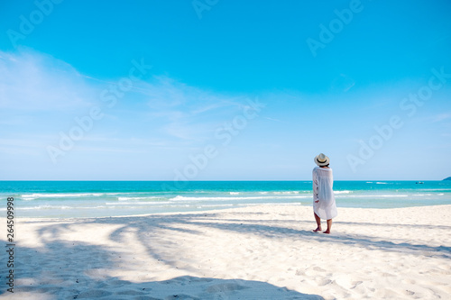 Fotografi A woman strolling on the beach with the sea and blue sky background