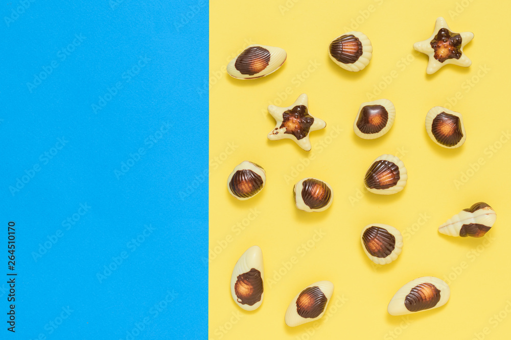 Fototapeta premium Chocolates in the form of sea shellfish and shells on a yellow and blue background. Flat lay.