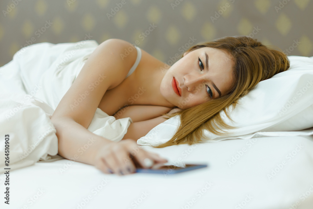 Young beautiful woman sleeps on the white background bed, wake-up and turn off cell phone alarm in the morning Young beautiful woman sleeps on the white background bed, wake-up and turn off cell phone alarm in the morning
