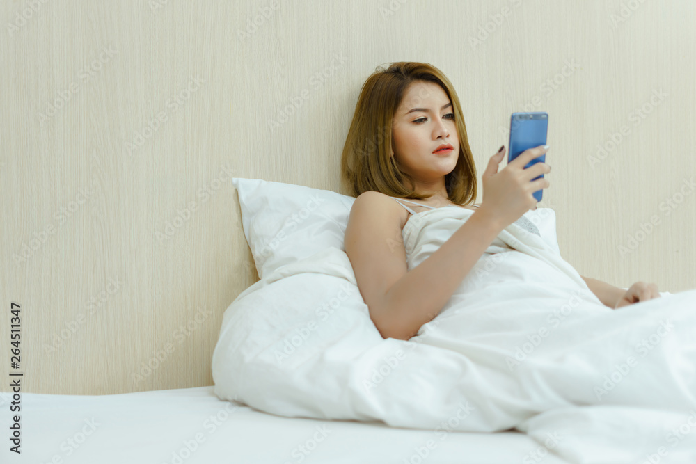 Young beautiful woman with long brown hair uses cell phone and relaxes on the white background bed. Young beautiful woman with long brown hair uses cell phone and relaxes on the white background bed.