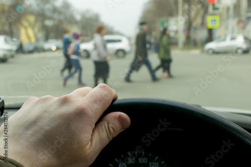 view from the car, the man's hand on the steering wheel of the car, located opposite the pedestrian crossing and pedestrians crossing the road