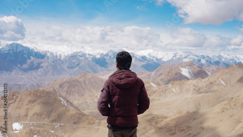 Back view of young man traveler in red jacket watching amazing beautiful mountain in Leh, Ladakh, India.