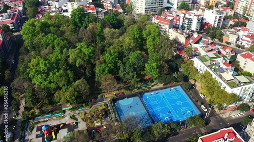 DRONE FLIGHT OVER PARK IN MEXICO CITY RESIDENTIAL AREA. KIDS PLAYGROUND COLORFUL, BLUE BASKETBALL COURT, AND CITY STABLISH photo