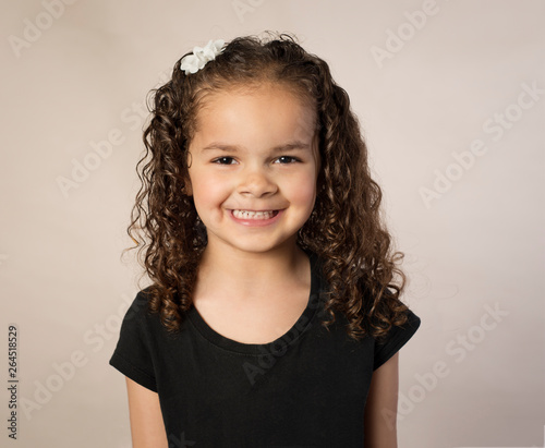 Biracial preschooler with curly brown hair isolated on brown background