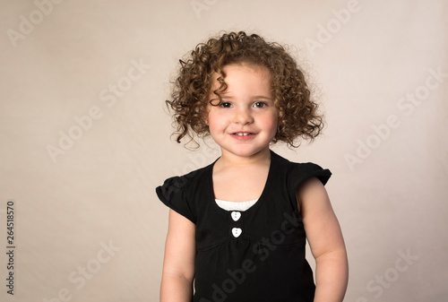 Smiling toddler with brown curly hair isolated on beige background photo