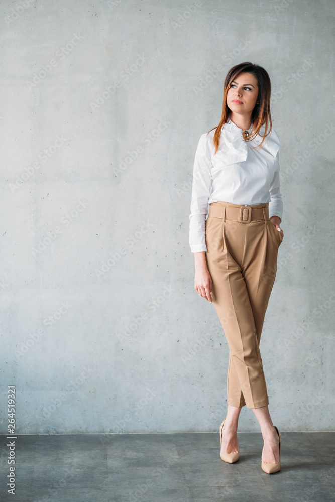 Successful business woman. Smart brunette young lady in formal outfit standing with legs crossed. Thoughtful facial expression.