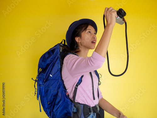 Searching for inspiring places. smiling adventure tourist woman with backpack and film camera taking photo isolated on yellow
