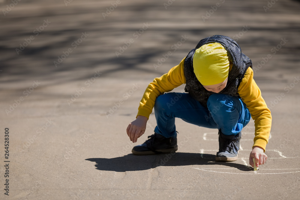 A little boy draws chalk hopscotch on the pavement or sidewalk. Creative child, fun activity. Games in the open air. Early development A little boy draws chalk hopscotch on the pavement or sidewalk. Creative child, fun activity. Games in the open air. Early development
