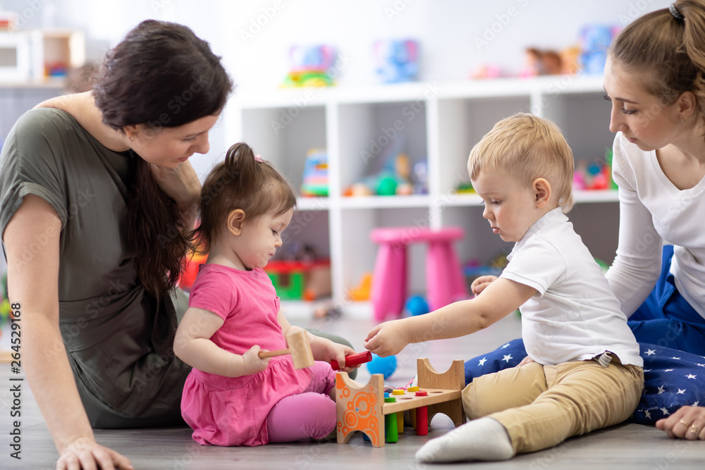 Group of babies playing together with mothers in the classroom in nursery or preschool Group of babies playing together with mothers in the classroom in nursery or preschool