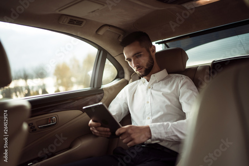 Man uses pc tablet sitting in back seat of car, businessman in taxi