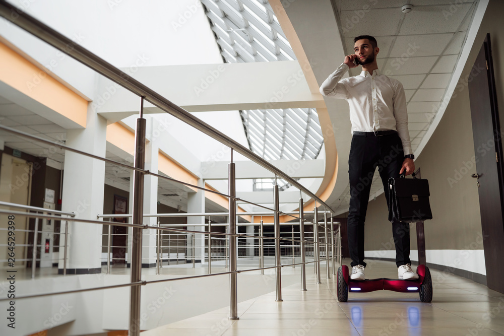 Young businessman is riding a gyroboard. He is talking on the smartphone Young businessman is riding a gyroboard. He is talking on the smartphone