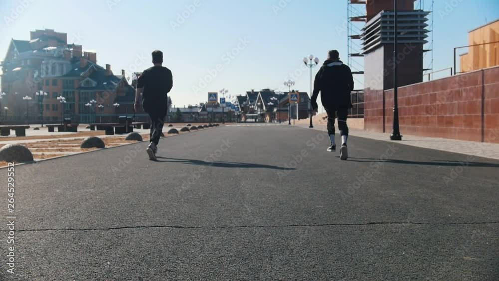 Urban streets. Two men running on the street and synchronously making tricks Urban streets. Two men running on the street and synchronously making tricks