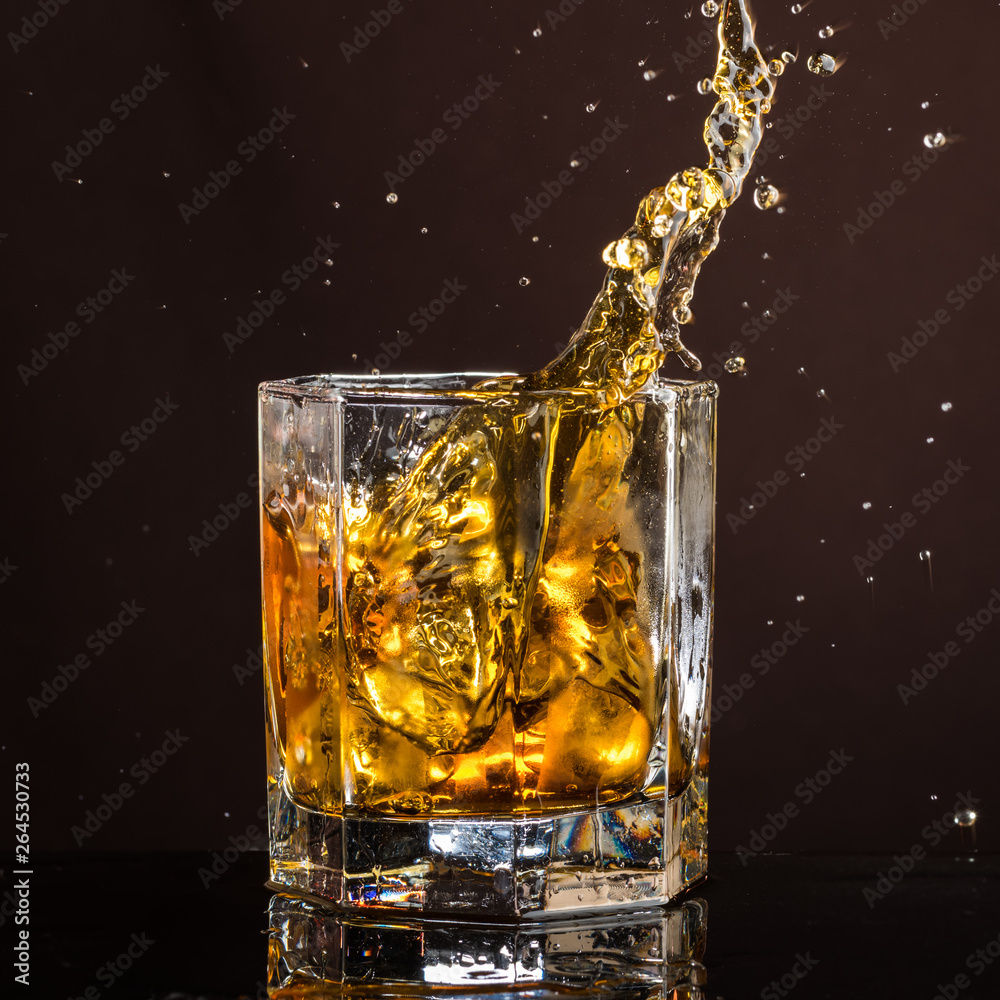 hexagonal glass of whiskey with ice and splashes from an abandoned and falling ice cube