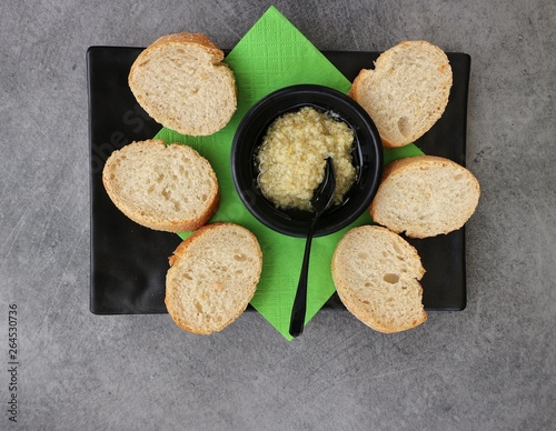 Horseradish and artichoke sauce in a black saucer with spoon and green napkin. Appetizer to spread on slices of bread.  Gray stone table on  background.