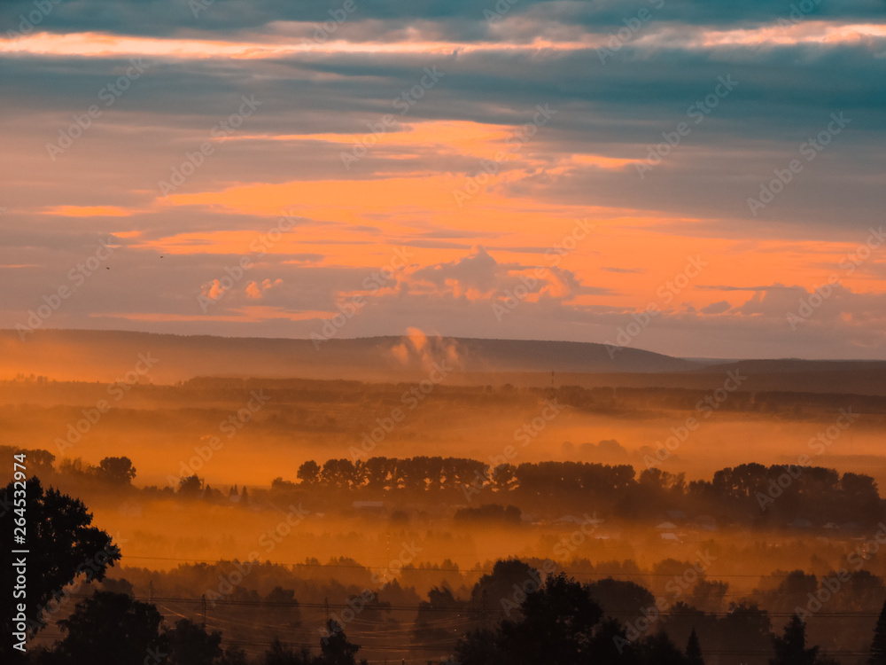 Fototapeta premium Beautiful landscape in the mountains at sunrise. Foggy nature. View of the foggy hills covered by forest. Sunny summer morning. Majestic sunset.Traveling concept background. Foggy background.