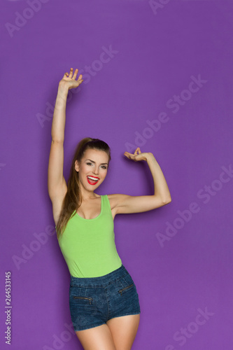 Happy Girl In Green Shirt And Jeans Shorts Is Holding Arms Raised And Laughing