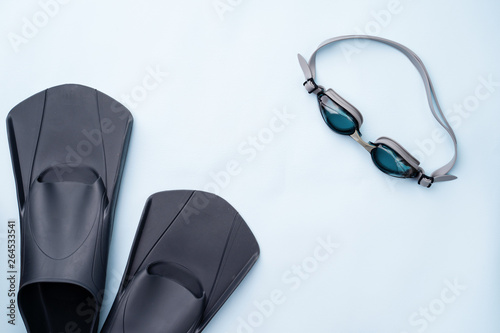 Swimming goggles and flippers on blue background.