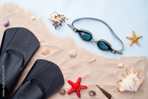 Swimming goggles and flippers on the sand with shells and starfishes.