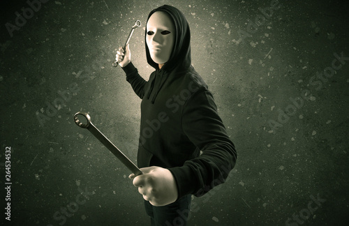 Tableau sur toile Masked armed villain in empty dark room with gun ax chainsaw mallet wrench