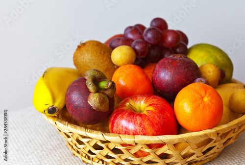 Bright tropical ripe fruits on a wicker plate  banana  orange  mango  grapes  tangerines  mangosteen  lychee  apple  pear  kiwi  lime. Healthy diet and low-calorie diet. Close-up  macro  copy space