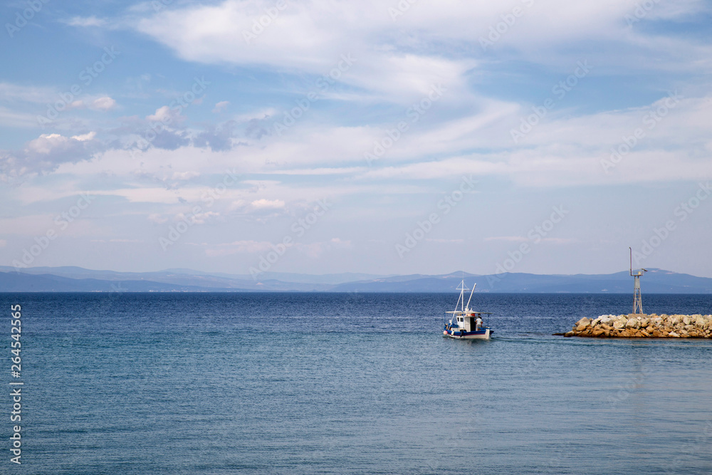 Small boat in blue sea approaching the harbor, tranquil blue sea with clouds in blue sky and fishing boat in summer, Halkidiki Greece