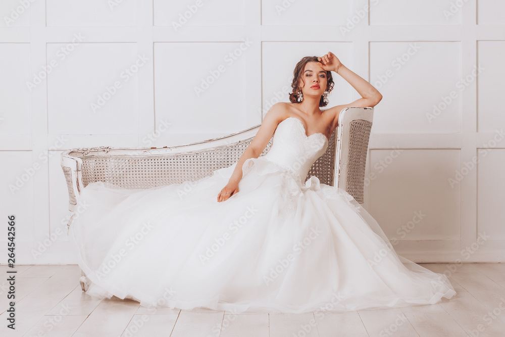 Young beautiful bride in a luxurious wedding dress sitting in a white room Young beautiful bride in a luxurious wedding dress sitting in a white room
