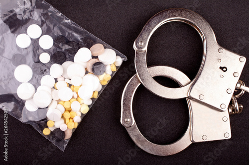 Handcuffs and drugs in a plastic bag on black background.