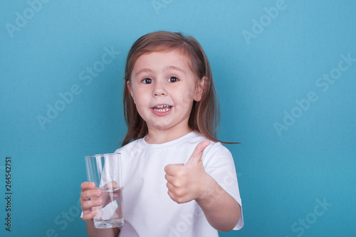 Cute little girl drinking water from glass on blue background