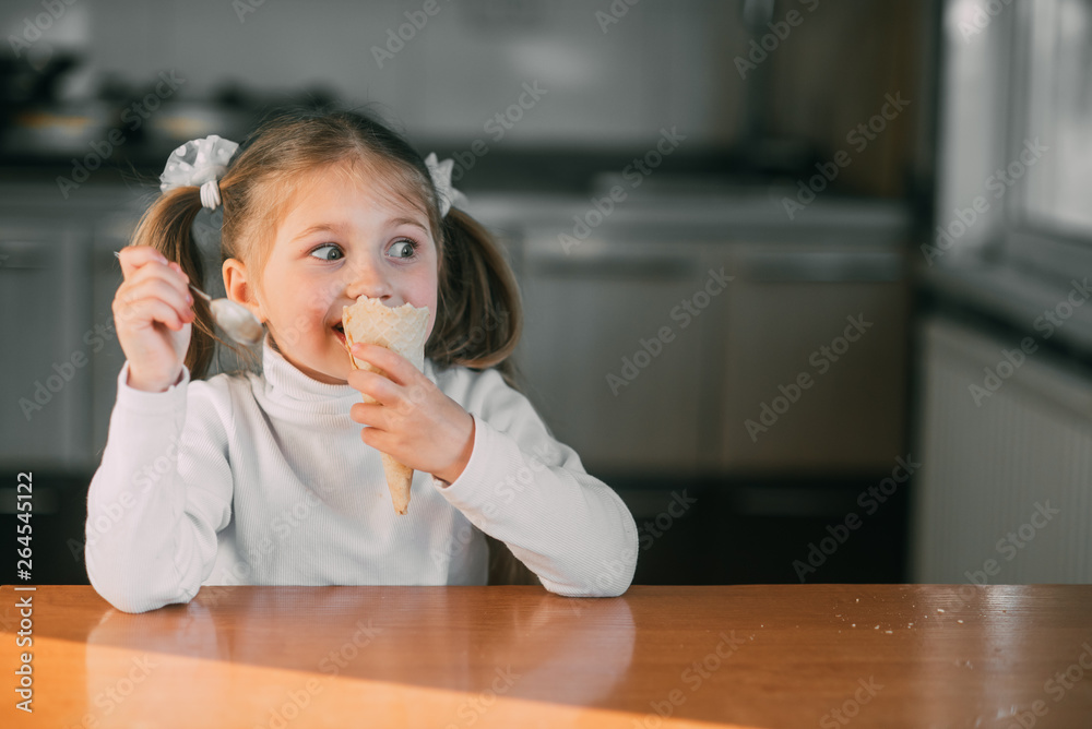 The girl in the kitchen eating the ice-cream cone with a spoon the light of day