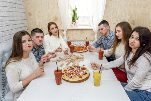 Friends play jenga, spit juice and eat pizza in cafe photo