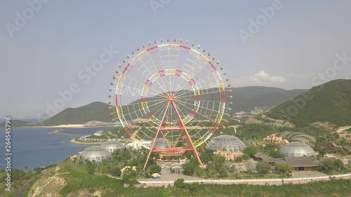 Colorful ferris wheel in amusement park on sea and mountain landscape aerial view. Amusement park with large ferris wheel view from from above flying drone.