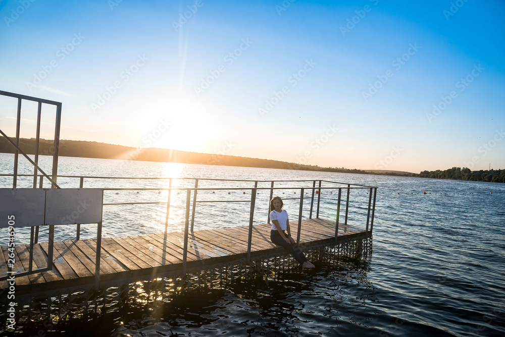 Woman sitting on pier against water and sunset