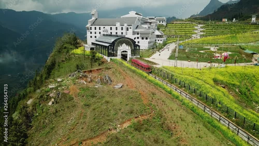 Epic overall railway red wagon rides into station on top of mountain. Modern french style building World Fansipan cable road funicular Sapa Vietnam landmark. Tourism Travel. Helicopter 