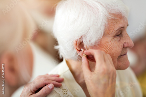 Female doctor applying hearing aid to senior woman's ear photo