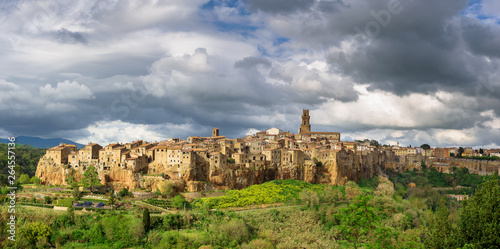 Green gorge with a medieval town on a hill and the blue sky in the background.