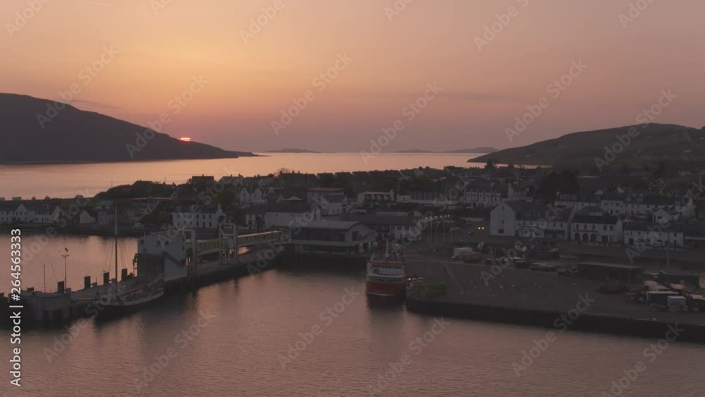Drone reveal shot of the sun setting behind Ullapool village on the north west Scottish Highlands. Ullapool is a fishing village located on the popular tourist route the NC500 north coast 500. Drone reveal shot of the sun setting behind Ullapool village on the north west Scottish Highlands. Ullapool is a fishing village located on the popular tourist route the NC500 north coast 500.