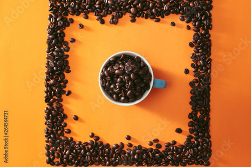 A full cup of coffee beans in the middle of quare shape coffee beans on orange background photo