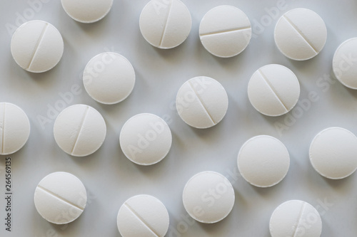 White roud pills scattered on white background, top view.