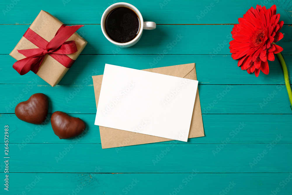 Romantic love concept. Flat lay composition with blank paper card, gift box, envelope, heart-shaped chocolate, flower, cup of coffee on pastel green background. Valentine day, anniversary.