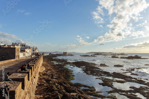 View of Essaouira at sunset. The old part of town is the UNESCO world heritage sites. Tourists and locals are enjoying the sunset at the old walls of Essaouira fortress in Morocco.