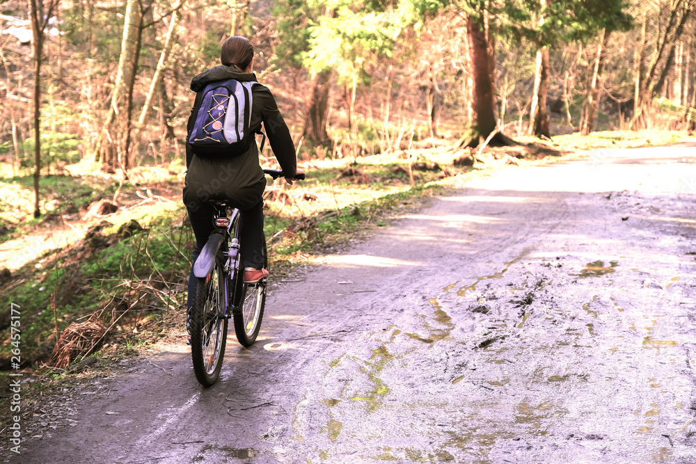 Obraz premium Girl tourist with a backpack riding a Bicycle on a forest road.
