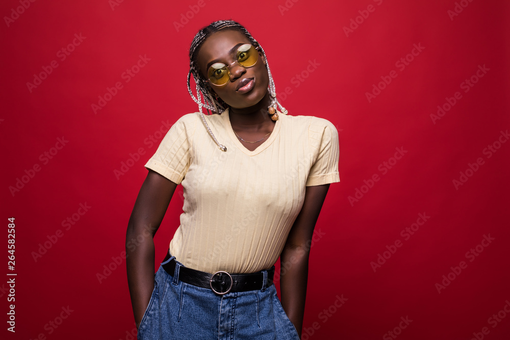 Terrific african model expressing surprised emotions while posing on indoor photoshoot. Stylish curly woman in sunglasses having fun in red background