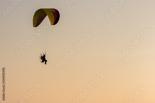 Silhouette of Paramotors flying to sky on sunset Adventure man active extreme sport pilot flying in sky with paramotor engine glider parachute. Paramotor flying on the sky at sunset. 