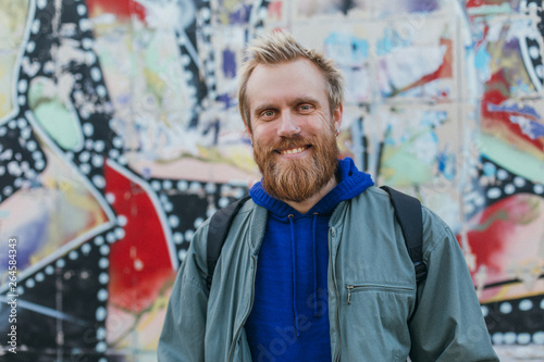 Cheerful nice young man isolated at colorful background. He pose on camera and smile. Positive man outside on street.